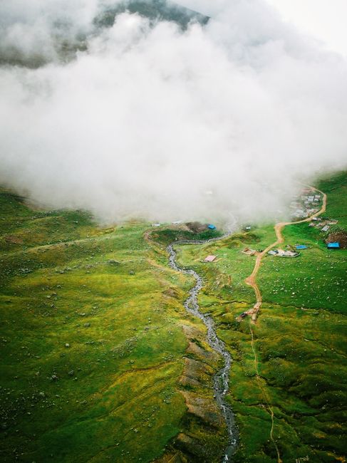 Dramatic aerial shot showcasing a lush green landscape with a winding stream, shrouded in fog.