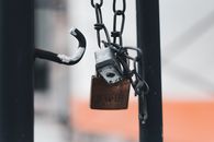 Close-up of a rusty padlock hanging on a metal chain with blurred background.