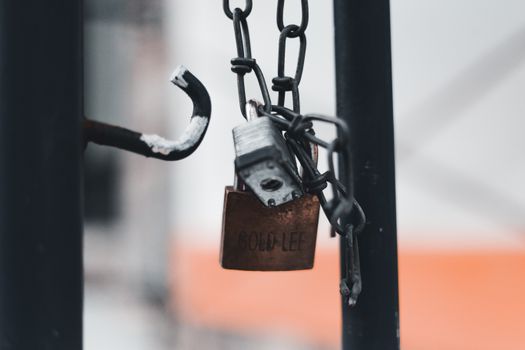 Close-up of a rusty padlock hanging on a metal chain with blurred background.