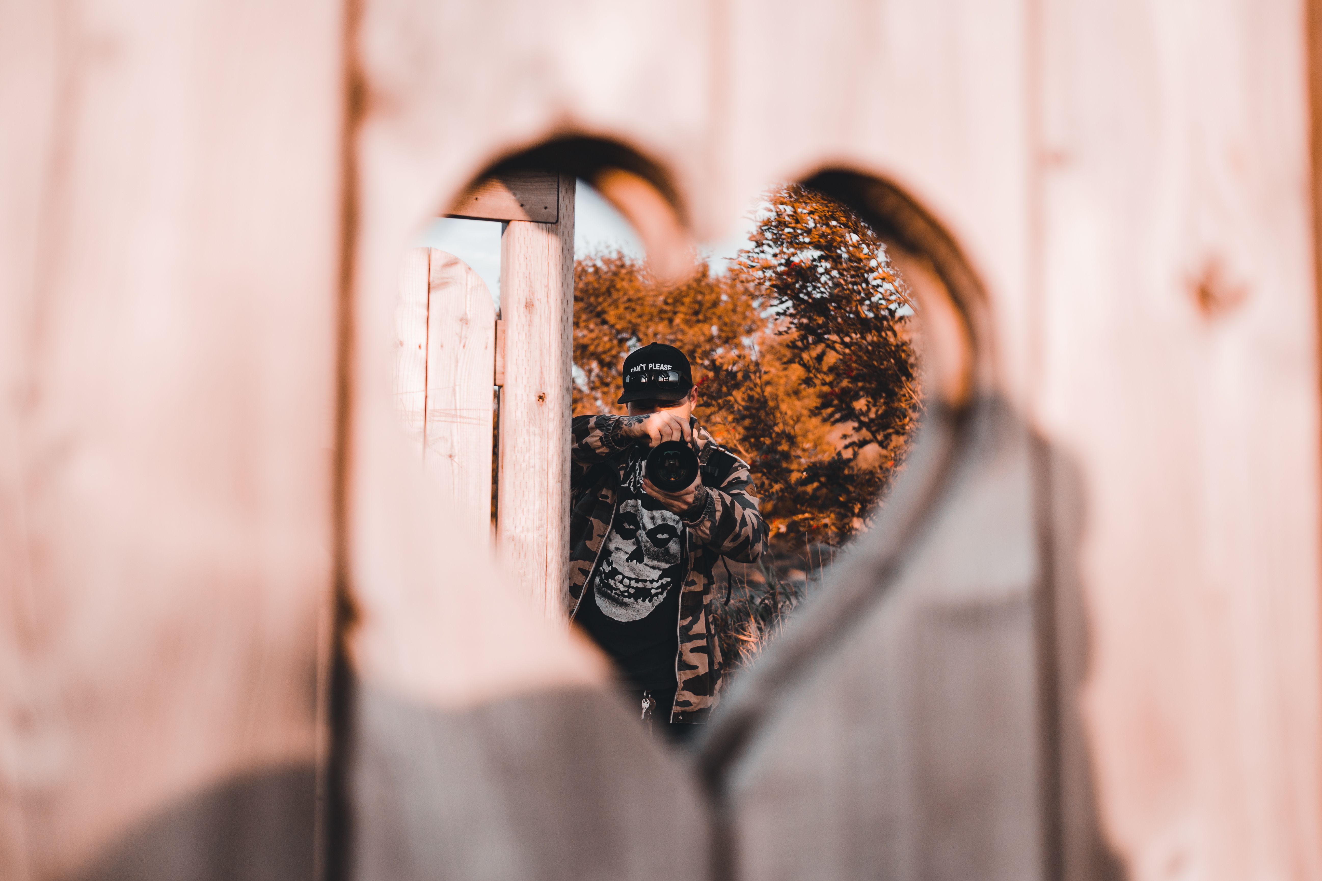 Photographer captured through a heart-shaped fence cutout, blending creativity and nature.