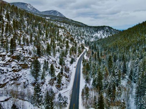 Free Aerial view of a snow-covered mountain highway in Colorado surrounded by pine trees. Stock Photo