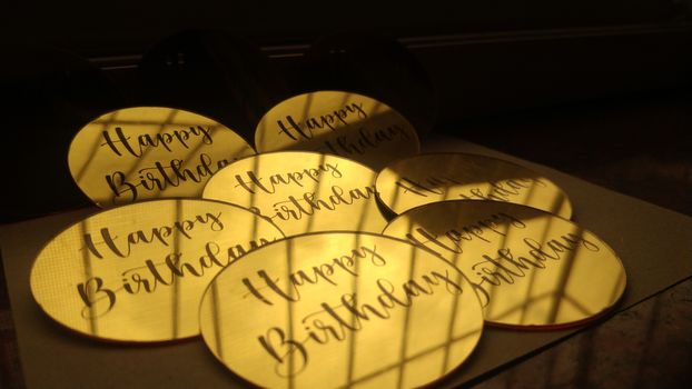 A collection of yellow Happy Birthday stickers illuminated by sunlight, casting shadows.