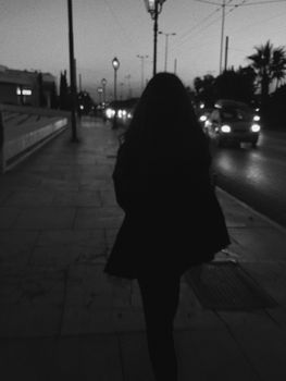 Silhouette of a woman walking on a city street at night, captured in monochrome.