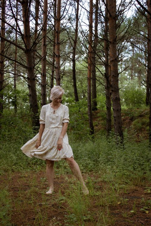 Free A woman in a white dress standing barefoot amidst tall pine trees in a peaceful forest setting. Stock Photo