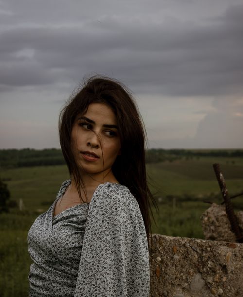 Free A brunette woman in a floral dress looks over her shoulder in a rural setting during twilight. Stock Photo