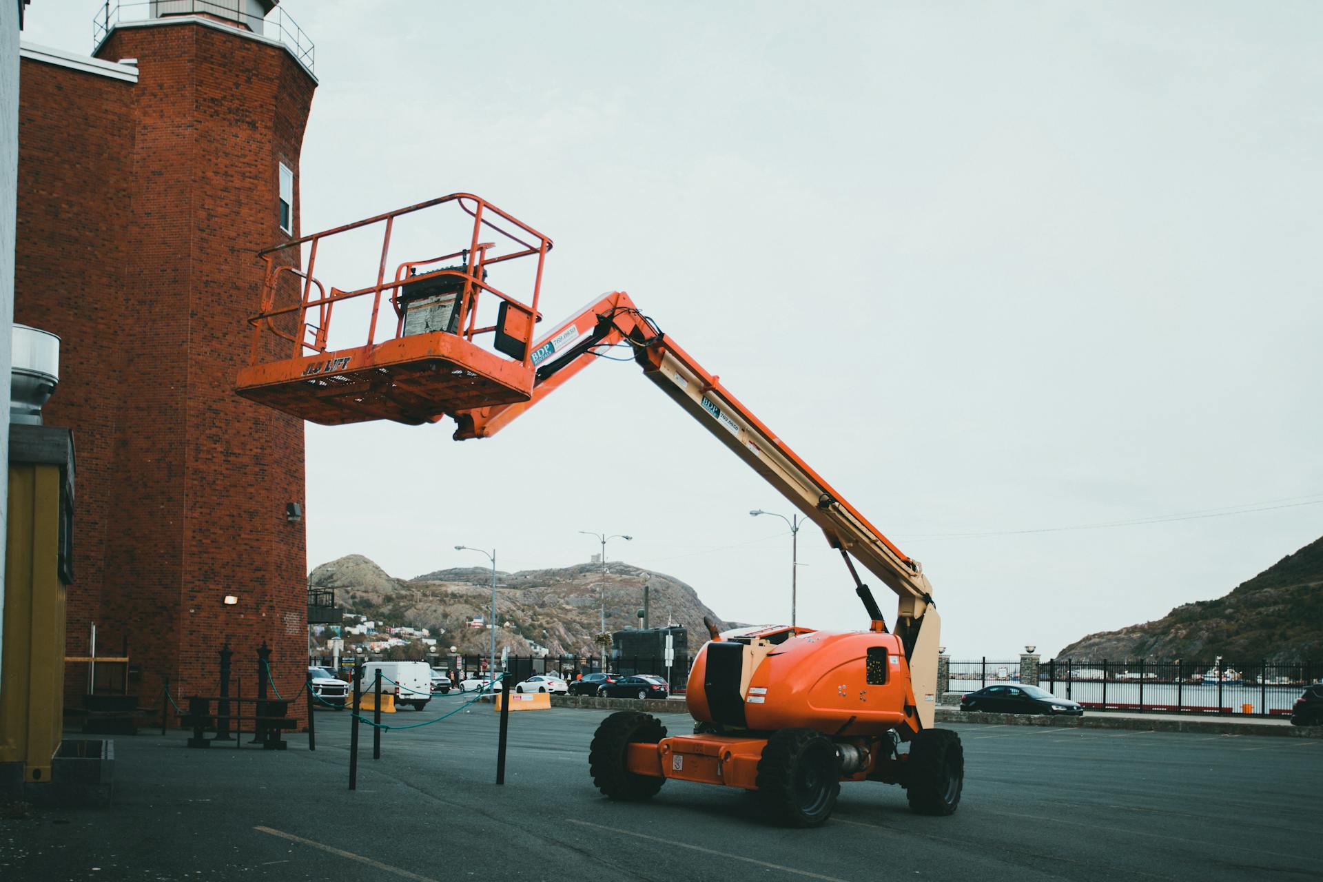 An orange boom lift positioned outdoors beside a brick building in an urban setting.