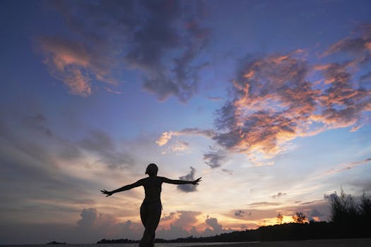 Silhouette of a woman embracing the vibrant sunrise on a beach in Phu Quoc, Vietnam, with dramatic clouds above.