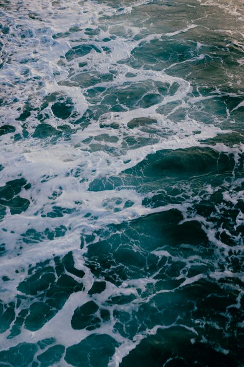 Free High angle shot of ocean waves and sea foam creating dynamic ripples in the sea. Stock Photo