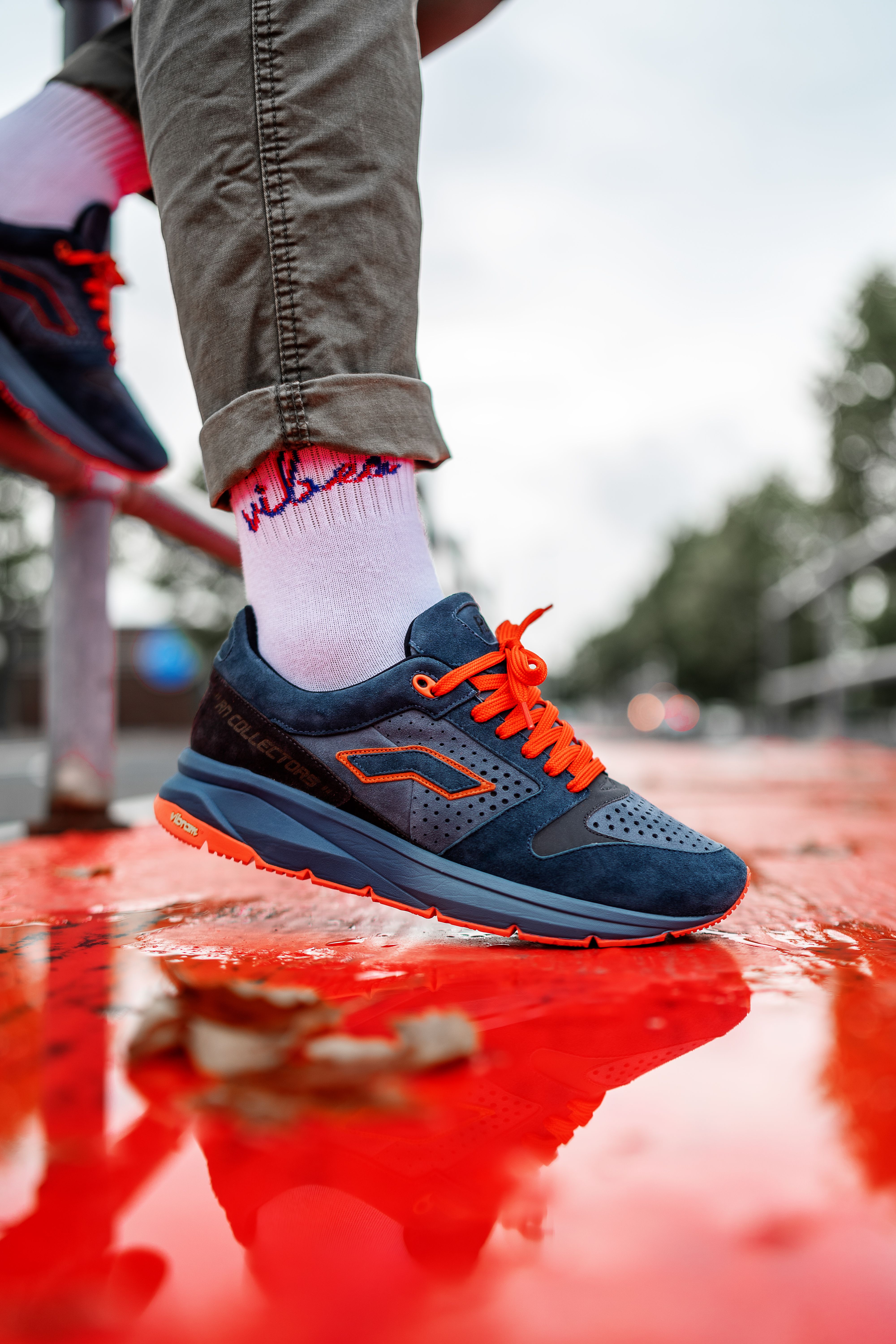 Close-up of a stylish blue and orange sneaker on a reflective red surface outdoors.