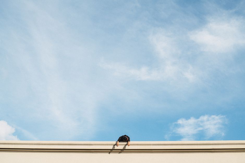 A person leans over a wall with a vibrant blue sky in the background. Minimalist composition.