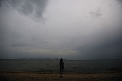 Free Moody image of a solitary figure standing by the misty beach under a gloomy sky at twilight. Stock Photo