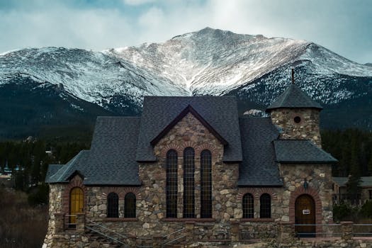 Beautiful stone chapel nestled against a snow-capped Rocky Mountain in Estes Park, Colorado.