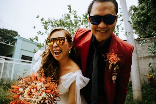 Happy couple in sunglasses smiling at their wedding with colorful bouquets.