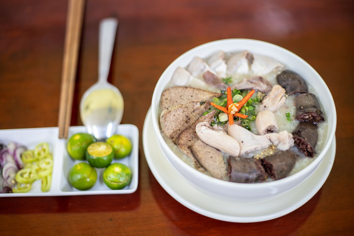 Bowl of rice congee with sliced pork, liver, blood cake and chili, beside limes and chilies