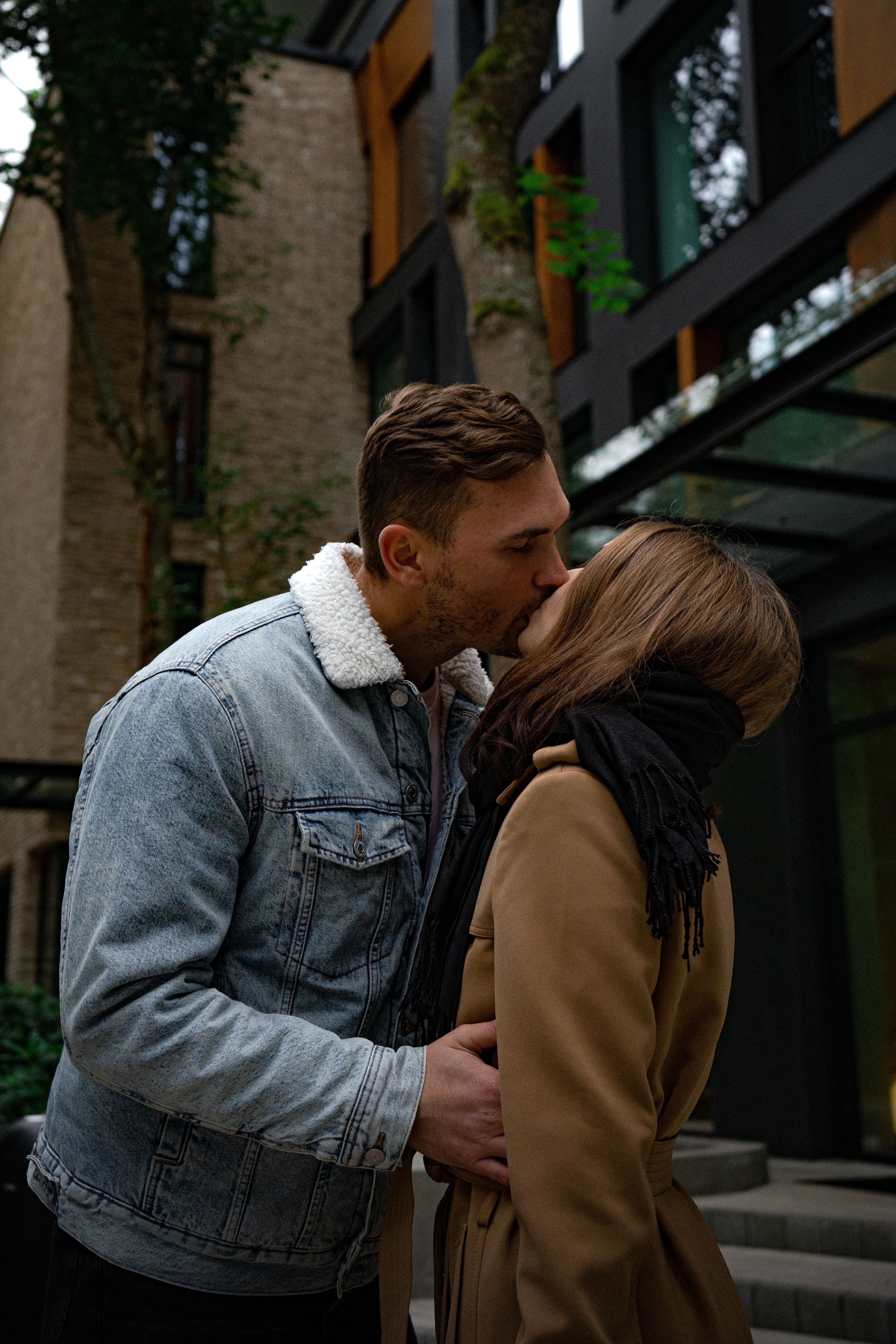 A Man in Denim Jacket Kissing a Woman Wearing a Brown Coat · Free Stock ...