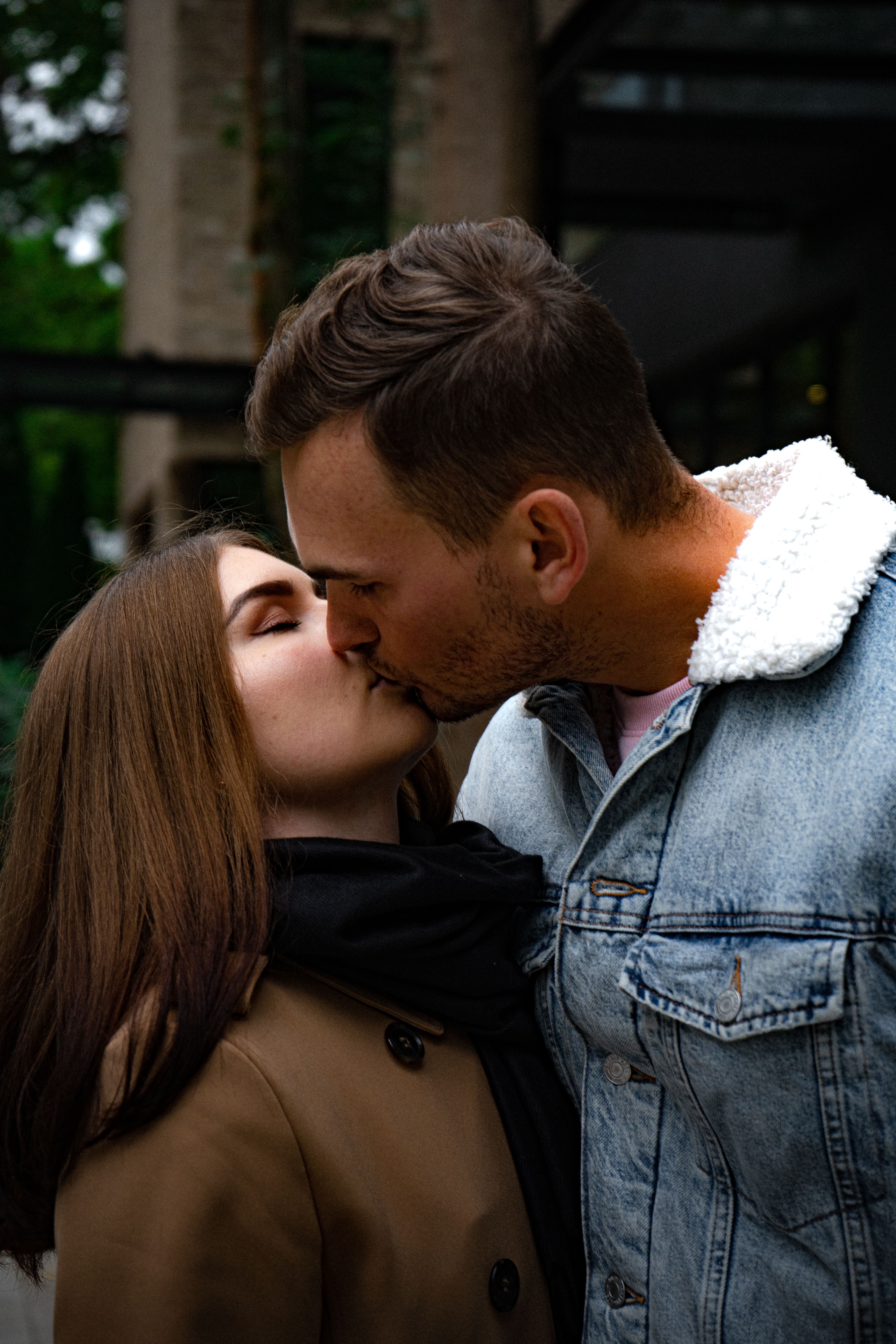 Man in Denim Jacket Kissing a Woman Wearing a Brown Coat · Free Stock Photo