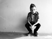 一个穿着黑白衣服、戴着眼镜的时尚小男孩蹲在墙上