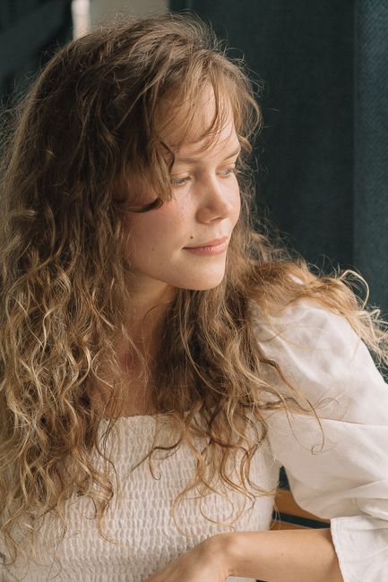 Elegant portrait of a woman with curly hair looking outside, capturing natural light and serene expression.