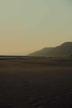 A tranquil beach scene at dusk with mountains in the background and a calm sea view.