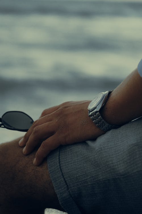 Free A Person in Gray Shorts Wearing a Wristwatch while Holding a Sunglass Stock Photo