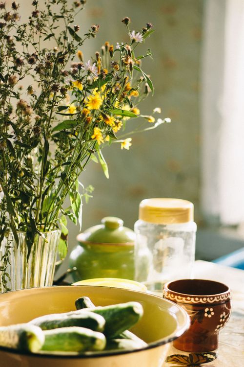 Free A rustic kitchen scene with cucumbers, wildflowers, and pottery in soft sunlight. Stock Photo