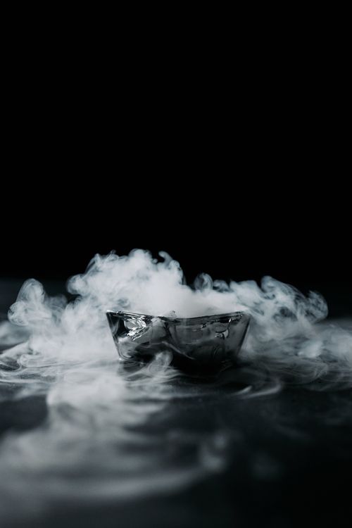 Free A mysterious scene with smoke emanating from a reflective metal bowl in a dark setting. Stock Photo