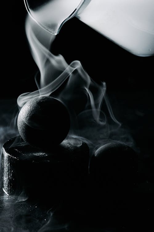 A Black Ball Surrounded by Smoke Coming Out from a Glass Pitcher