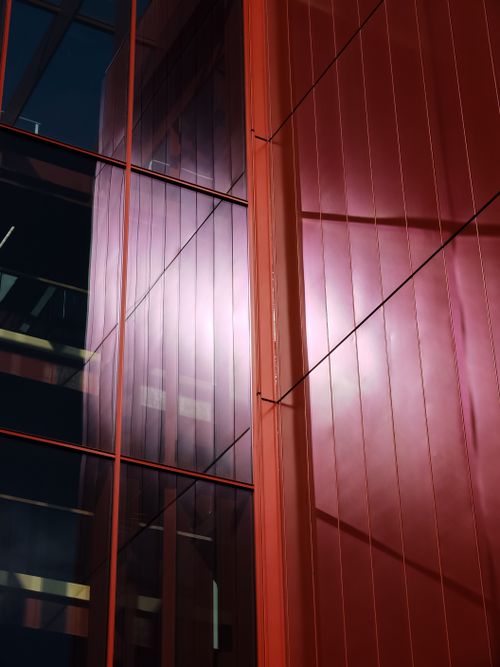 Free A striking view of modern architecture with reflective glass panels and red hues, capturing futuristic design. Stock Photo