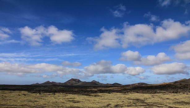 Expansive desert scene featuring arid mountains under a bright blue sky with scattered clouds.