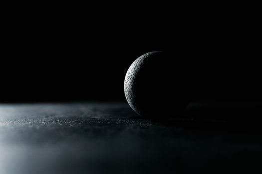 A dark moody still life of a textured sphere on a black surface, creating dramatic lighting effects.