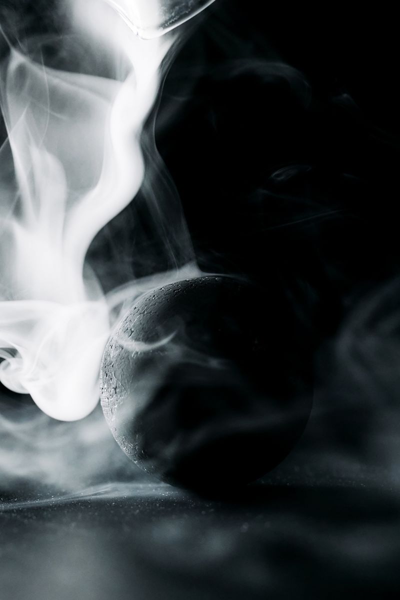 A dramatic black sphere enveloped by swirling white smoke on a dark background.