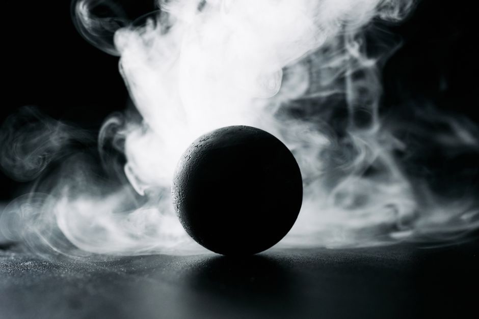 A dark sphere surrounded by swirling smoke creates a mysterious and dramatic scene.
