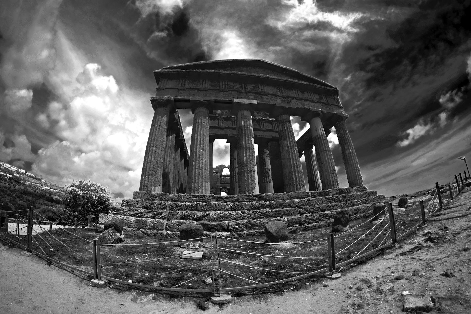 A captivating black and white image of ancient temple ruins with dramatic clouds overhead, showcasing historical architecture.