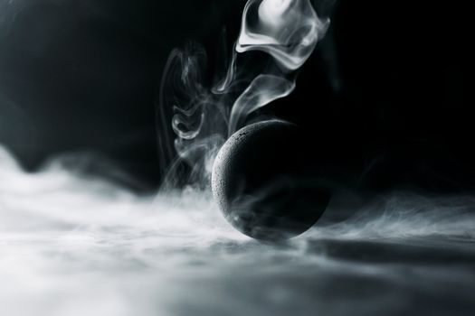 Abstract image of a black sphere engulfed in swirling, mysterious smoke.