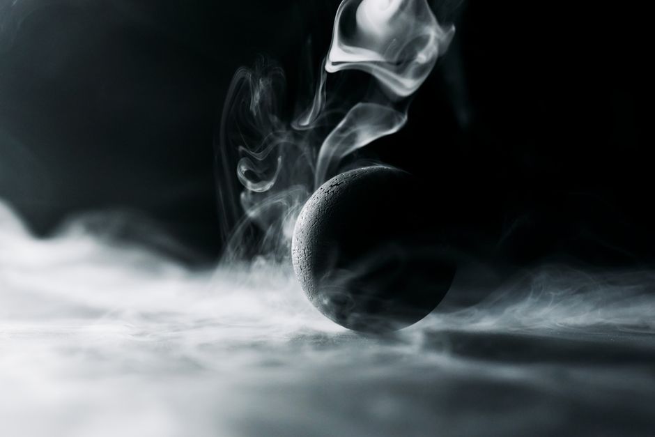 Abstract image of a black sphere engulfed in swirling, mysterious smoke.