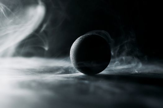 Dark spherical object surrounded by swirling smoke in a dramatic atmosphere.
