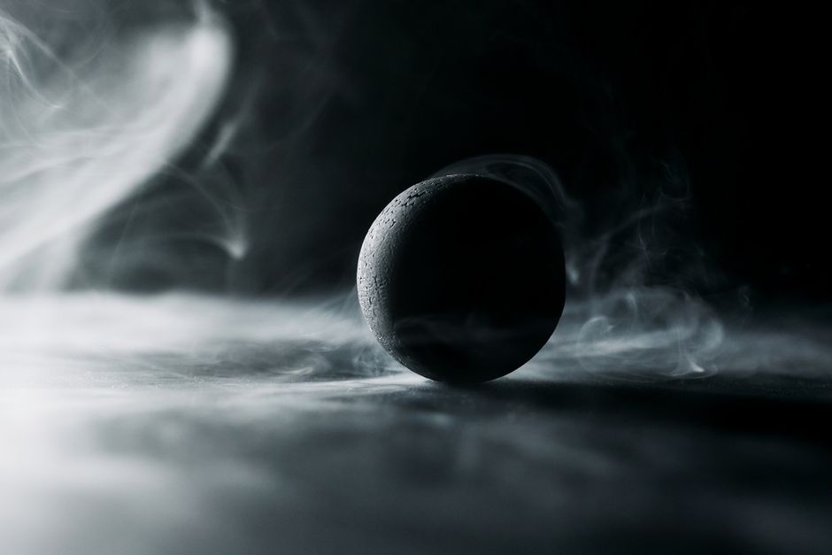 Dark spherical object surrounded by swirling smoke in a dramatic atmosphere.