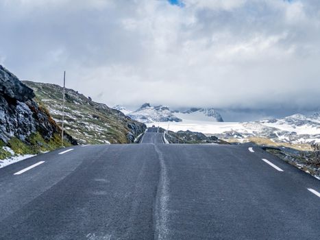 A picturesque road leading through snow-covered mountains under a cloudy sky.