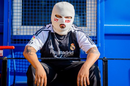 Free A person wearing a ski mask and sports jersey sits in an urban outdoor setting. Stock Photo