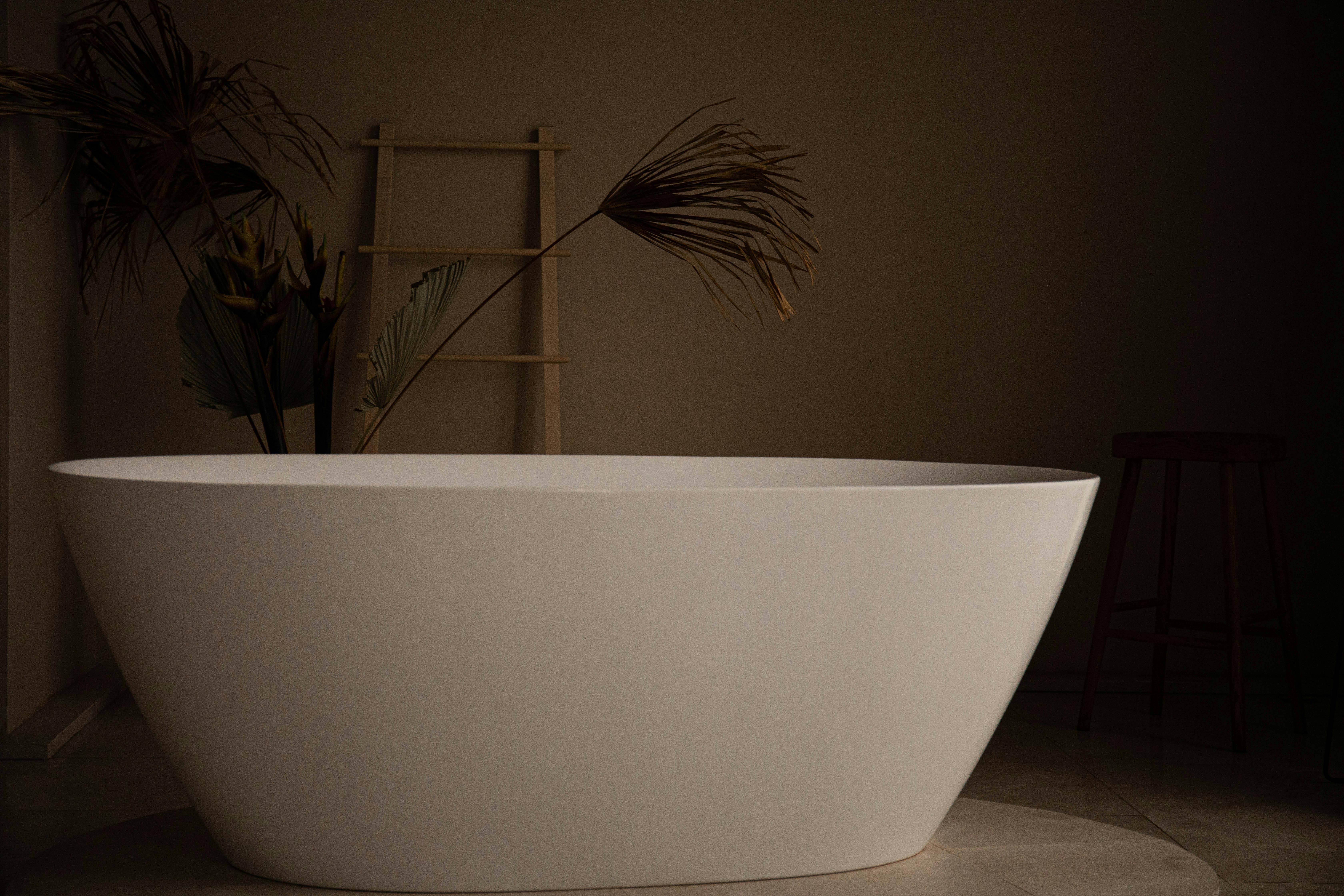 Elegant freestanding bathtub in a modern bathroom with plants and a wooden ladder.