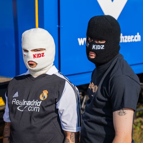 Free Two adults wearing knit masks and branded apparel in an outdoor setting. Stock Photo