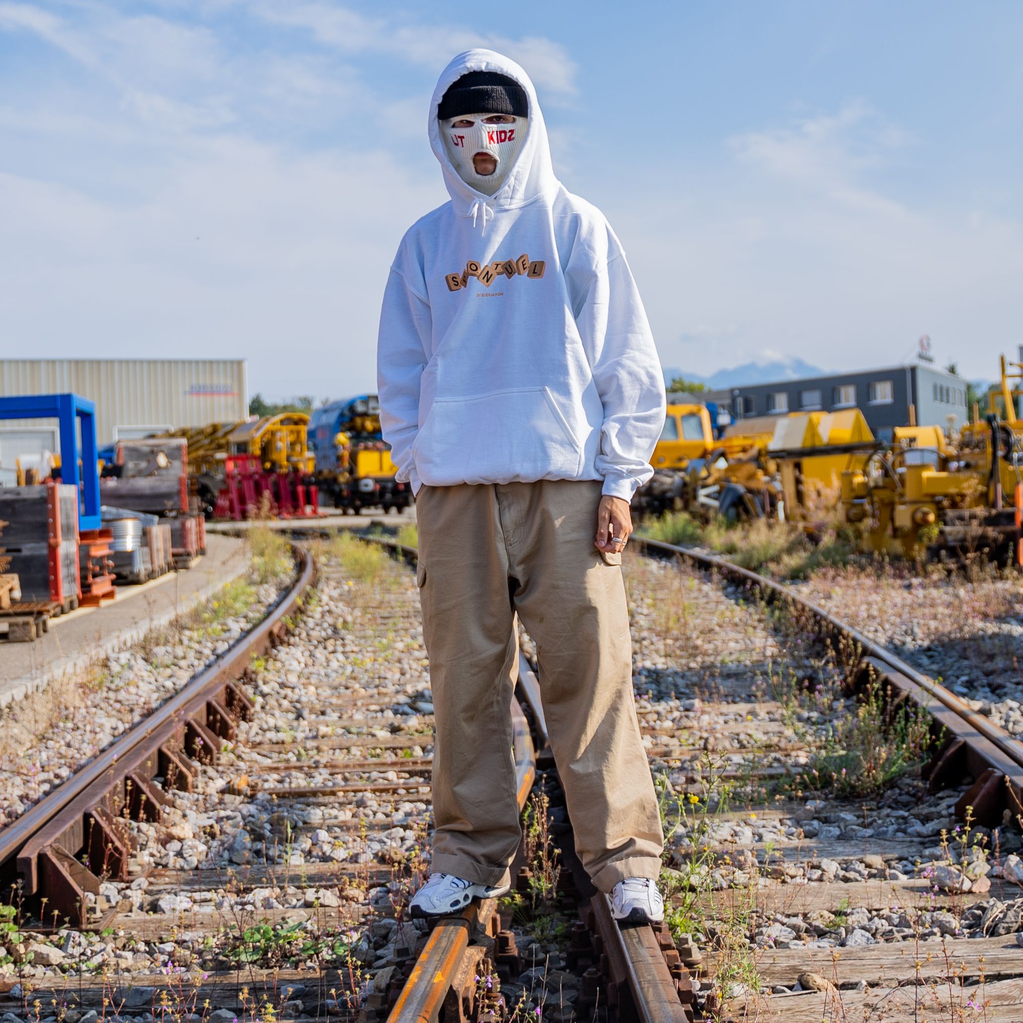 Street style photo of a person in a hoodie and mask on train tracks in Lausanne.