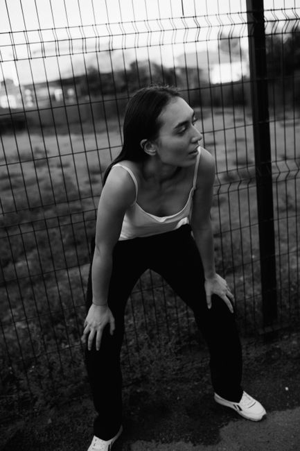 Black and white portrait of a woman leaning against a metal fence outdoors.