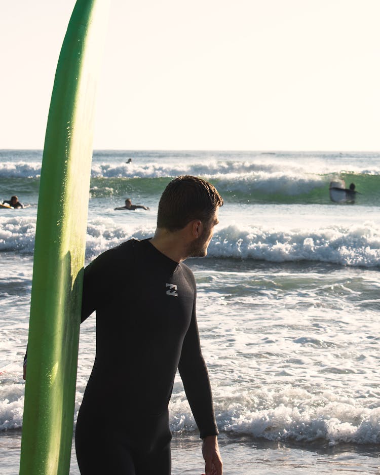 A Man In Black Swimwear Holding A Green Surfboard