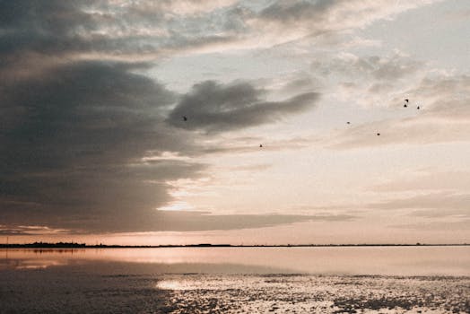 A tranquil beach scene at sunset with dramatic clouds and calm waters.
