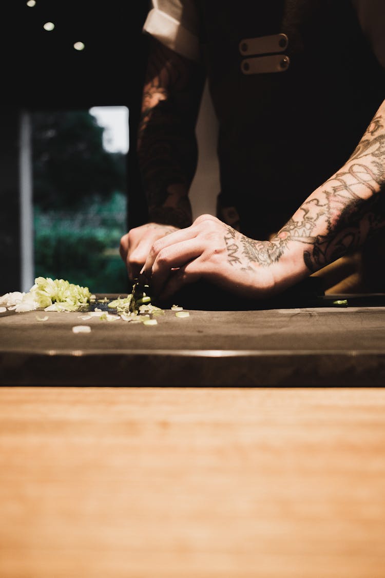 A Tattooed Person Cutting Scallions