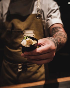 Close-up of a chef with tattoos holding sushi hand roll in dim lighting, capturing the essence of Japanese cuisine.
