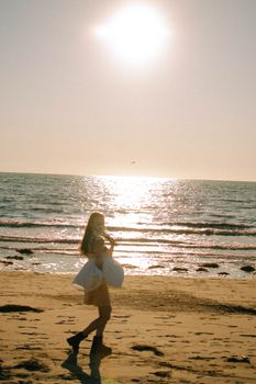 A woman walks along a sunlit beach, the ocean waves glistening in the warm afternoon light.