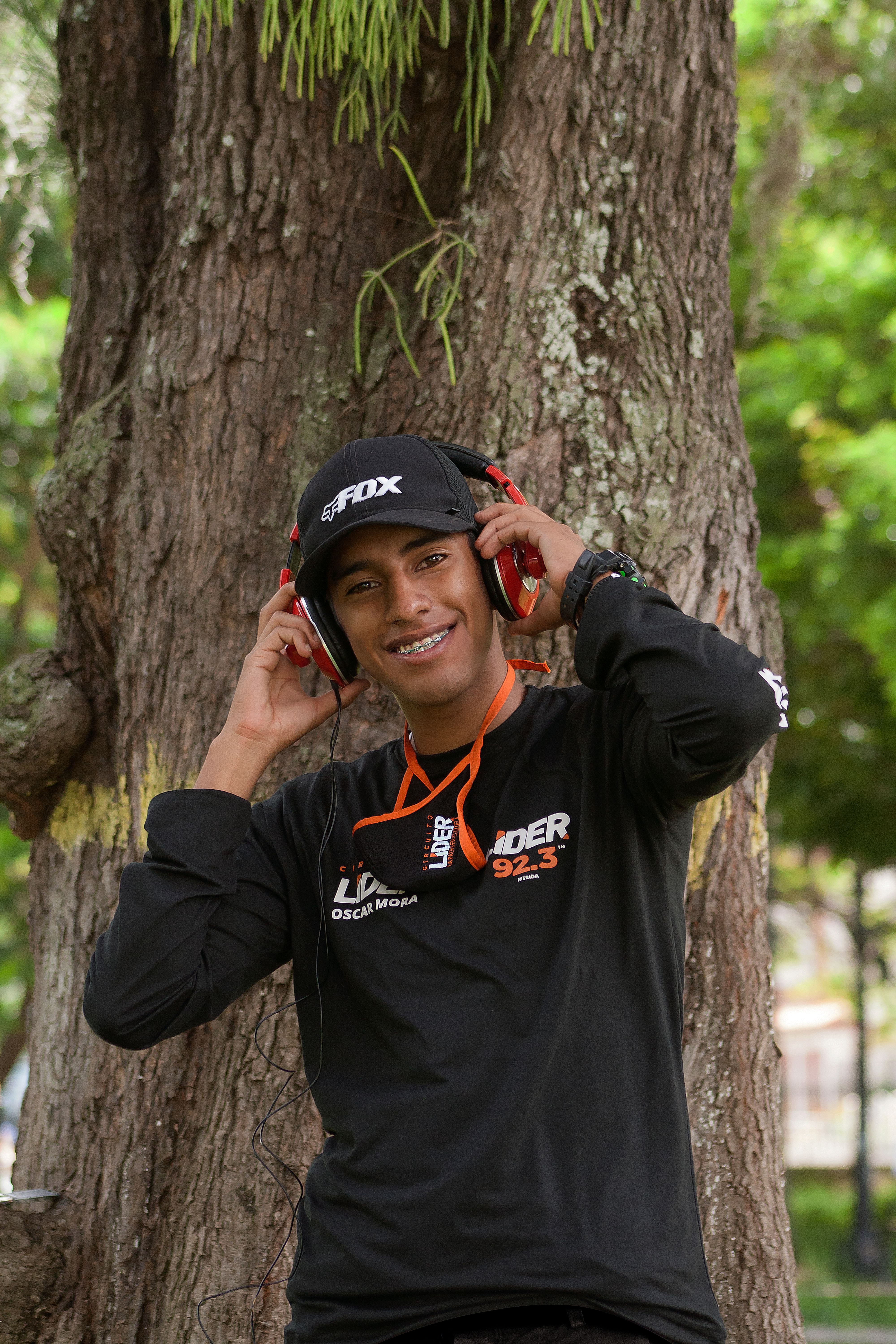 A cheerful young man in sportswear enjoying music with headphones outdoors in a green park setting.