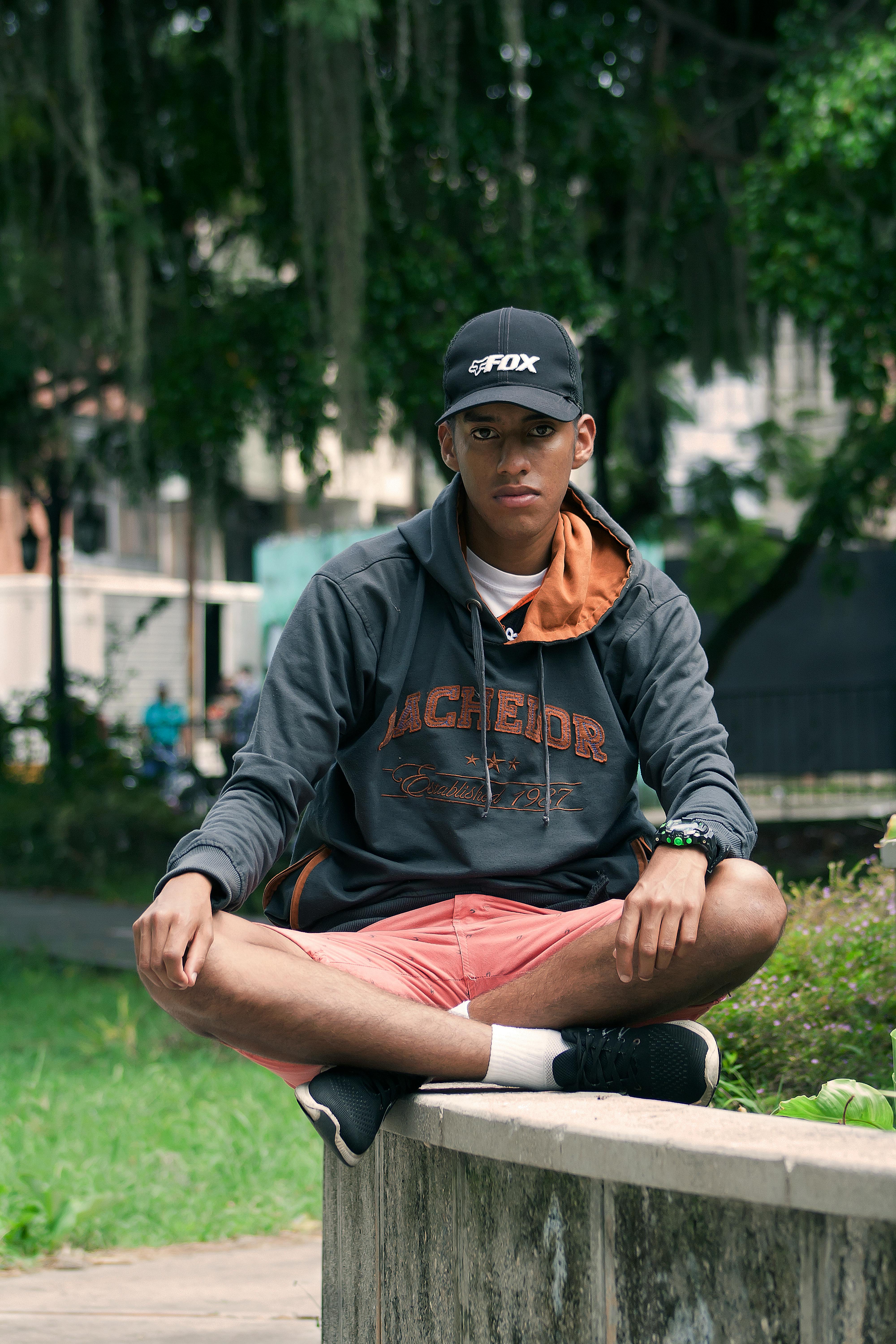 Young adult man wearing casual clothes sitting on a wall in a Venezuelan park.